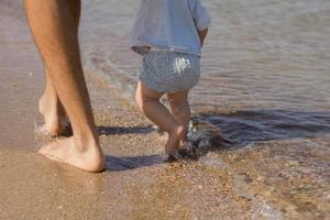 Nahaufnahme des Vaters mit einem einjährigen Kind, das im Sommer am Strand spazieren geht foto