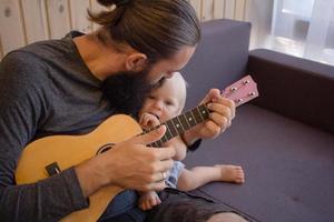 bärtiger vater mit kindern spielen auf ukulele drinnen foto