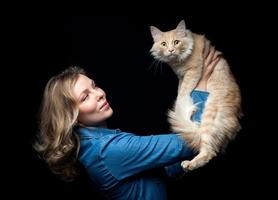 Schöne Besitzerin, die mit ihrer Katze auf schwarzem Hintergrund posiert foto