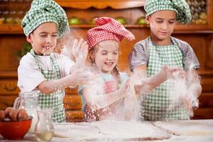 drei lustige kleine Kinder, die Hände mit Mehl in der Küche schütteln