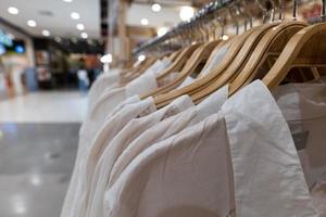 Weiße Kleider hängen an Holzständern. Kleidung für Frauen, die im Einkaufszentrum zum Verkauf an Kleiderbügeln hängen. foto