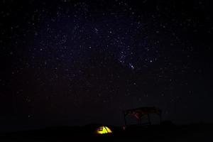 Ein gelb beleuchtetes Zelt steht in der Dunkelheit am Campingtisch mit magentafarbenem Himmelshintergrund foto