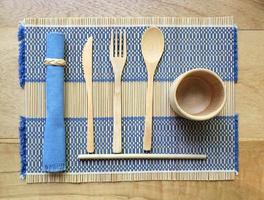 Bambusholzbesteck, Einweggabel, Löffel, Messer, Strohhalm und Bambusbecher aus Naturmaterial auf Tischset foto
