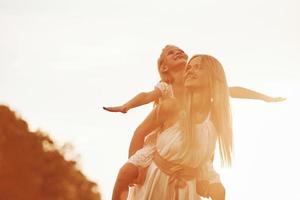 auf den Schultern der Frau sitzen. mutter und tochter genießen das gemeinsame wochenende, indem sie draußen auf dem feld spazieren gehen. schöne Natur foto