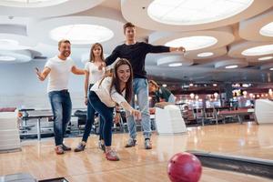 Komm schon, du kannst es. Junge, fröhliche Freunde haben an ihren Wochenenden Spaß im Bowlingclub foto