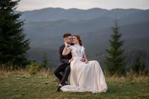 Fröhliche stilvolle Braut und Bräutigam, die an sonnigen Sommertagen in den Bergen laufen und Spaß haben foto