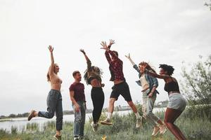 versuchen ihr Bestes, um so hoch wie möglich zu springen. gruppe von menschen picknickt am strand. Freunde haben Spaß am Wochenende foto