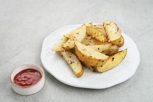 Geröstete Kartoffelecken mit Rosmarin und Kräutern, serviert mit Chilisauce foto