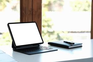 Mockup-Bild eines schwarzen digitalen Tablet-PCs mit leerem weißen Desktop-Bildschirm auf dem Arbeitsplatz im Heimbüro foto