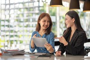 Zwei junge asiatische Geschäftsfrauen unterhalten sich in einer Gruppensitzung am Bürotisch in einem modernen Bürointerieur. Business Collaboration Strategische Planung und Brainstorming von Mitarbeitern foto