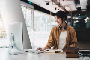 hipster asiatische mädchen schülerin mit tragen kopfhörer notizen schreiben video online webinar ansehen auf laptop lernen im bett sitzen elearning kurs videokonferenz pc anruf im schlafzimmer zu hause foto