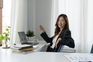 charmante asiatische Geschäftsfrau, die mit einem Laptop im Büro arbeitet. Blick in die Kamera foto