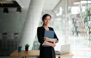 Portrait Vertrauen Business Asiatin stehend während der Arbeit für die Finanzbuchhaltung mit Laptop und Taschenrechner foto