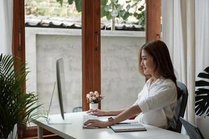 Seitenansicht der charmanten, intelligenten asiatischen Unternehmerin, die ein Karriereentwicklungsseminar für Computerarbeitstrainingsunternehmen im Home Office verwendet. foto