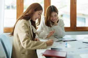 Zwei asiatische Geschäftsfrauen und Partner, die Taschenrechner und Laptop für die Berechnung von Finanzen, Steuern, Buchhaltung, Statistiken und analytischen Forschungskonzepten verwenden foto