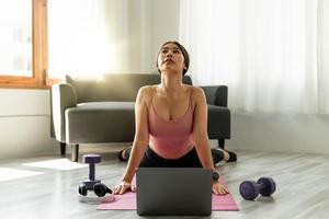 Fitnesstrainer mit virtuellem Yoga-Kurs per Videoanruf auf dem Laptop. Remote-Yoga-Lehrer leitet eine Lektion für Menschen foto