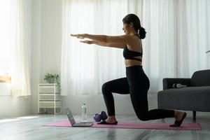 fitte sportliche junge asiatin online-trainingsübung zu hause. aktives gesundes Mädchen genießt Sport Pilates Yoga Fitnesstraining auf Laptop-Computer Stretching auf Yogamatte Videoklasse ansehen foto