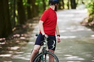 Ich hörte das Auto dahinter. Radfahrer auf dem Fahrrad ist an sonnigen Tagen auf der Asphaltstraße im Wald foto