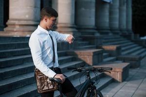 Zeit zu gehen. Geschäftsmann in formeller Kleidung mit schwarzem Fahrrad ist in der Stadt foto