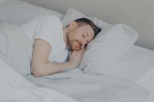 hübscher junger mann, der bequem zu hause im bett schläft foto