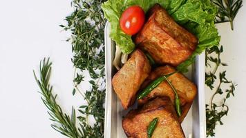 Gebratener Tofu, kleine Tomaten und grüne Chilischoten zusammen mit Salat in einem Aluminiumbehälter, indonesisches Straßenessen auf weißem Hintergrund foto