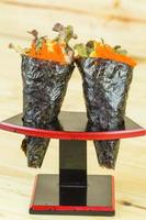 isolierter ikura lachsrogen und kani mit avocado, tamago yaki japanisches spiegelei und ebiko garnelenei kalifornien oder temaki sushi handrolle auf holzständer. foto