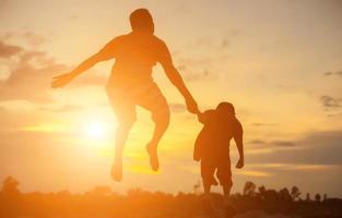 Glücklicher Vater wirft das Baby bei Sonnenuntergang foto