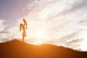 Silhouetten von Mutter und kleiner Tochter, die bei Sonnenuntergang spazieren gehen foto