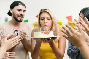 schönes mädchen, das den geburtstagskuchen auf der party mit freunden bläst, klatscht ihr geburtstagsfeierlied. foto