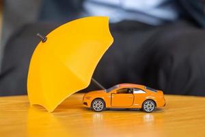 gelbe regenschirmabdeckung oder schutz orangefarbenes autospielzeug auf dem tisch. finanz-, geld-, refinanzierungs- und autoversicherungskonzept foto