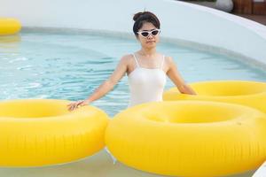 glückliche frau im weißen badeanzug mit gelbem schwimmring im luxus-poolhotel, junge frau mit sonnenbrille genießt im tropischen resort. entspannendes, sommerreise-, urlaubs-, urlaubs- und wochenendkonzept foto