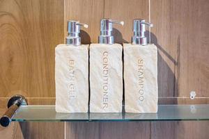 toilettenartikelflaschen im badezimmer im luxushotel oder im modernen haus. duschbehälterset, körperduschgel, shampoo und haarspülung aus keramik mit holzwandhintergrund foto