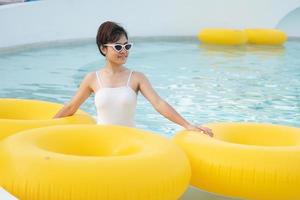 glückliche frau im weißen badeanzug mit gelbem schwimmring im luxus-poolhotel, junge frau mit sonnenbrille genießt im tropischen resort. entspannendes, sommerreise-, urlaubs-, urlaubs- und wochenendkonzept foto