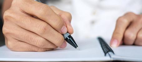 Geschäftsfrau schreibt etwas auf Notizbuch im Büro oder Café, Hand der Frau hält Stift mit Unterschrift auf Papierbericht. Geschäftskonzepte foto