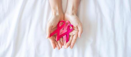 oktober brustkrebsbewusstseinsmonat, hand einer erwachsenen frau, die rosa band auf rosa hintergrund hält, um lebende menschen und krankheit zu unterstützen. internationales frauen-, mutter- und weltkrebstagskonzept foto
