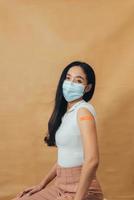 asiatische frau, die schultern zeigt, nachdem sie einen impfstoff erhalten hat. glückliche Frau, die nach der Impfinjektion einen Arm mit Pflastern zeigt. foto