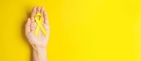 Hand, die ein gelbes Band auf gelbem Hintergrund hält, um Menschen zu unterstützen, die leben und krank sind. Tag der Suizidprävention im September, Monat des Bewusstseins für Krebs im Kindesalter und Konzept des Weltkrebstages foto