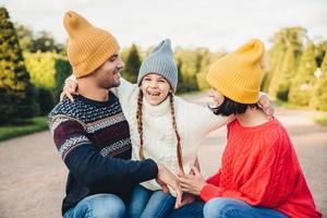 glückliches kleines mädchen umarmt ihre mutter und ihren vater, hat spaß zusammen, geht im schönen park oder auf der straße spazieren. eltern sehen ihre schöne tochter an und versuchen, das beste für sie zu tun. Glückliche Familie erholt sich gut im Freien foto