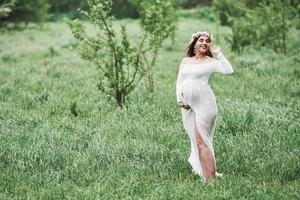 schöne Naturgeräusche. Schöne schwangere Frau im Kleid macht einen Spaziergang im Freien. positive Brünette foto