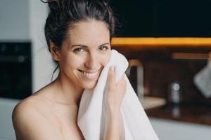 kaukasische frau wischt gesicht mit handtuch ab und lächelt. Hygiene, Dermatologie und Hautreinigung. foto