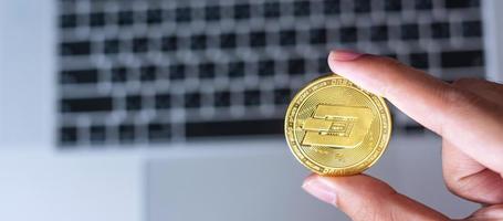 Geschäftsmannhand, die goldene Dash-Kryptowährungsmünze über Tastatur-Laptop hält, Krypto ist digitales Geld innerhalb des Blockchain-Netzwerks foto