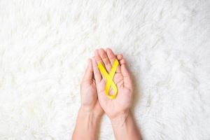 Hand, die gelbes Band auf weißem Hintergrund hält, um das Leben und die Krankheit von Menschen zu unterstützen. Tag der Suizidprävention im September, Monat des Bewusstseins für Krebs im Kindesalter und Konzept des Weltkrebstages foto