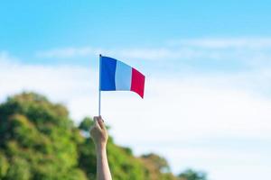 Hand, die Frankreich-Flagge auf Hintergrund des blauen Himmels hält. feiertag des französischen nationaltages, bastille-tag und fröhliche feierkonzepte foto