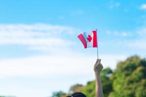 Hand, die Kanada-Flagge auf Hintergrund des blauen Himmels hält. kanada-tag und fröhliche feierkonzepte foto