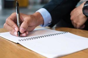 Geschäftsmann im Anzug schreibt etwas auf Notizbuch im Büro oder Café, Hand des Mannes hält Stift mit Unterschrift auf Papierbericht. Geschäftskonzepte foto