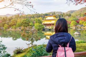 alleinreisende touristin, die in der herbstsaison im kinkakuji-tempel oder im goldenen pavillon unterwegs ist, asiatischer reisender besucht in kyoto, japan. urlaub, ziel und reisekonzept foto