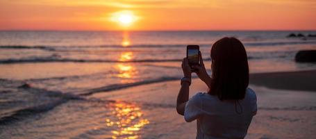 Silhouette einer glücklichen jungen Frau, die ein Foto per Smartphone macht. Touristen genießen den wunderschönen Sonnenuntergang am Strand. reisen, entspannen, urlaubssommerkonzept