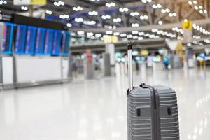 Gepäcktasche im internationalen Flughafenterminal, Trolley-Koffer mit Informationstafel im Flugplatzhintergrund. Transport-, Versicherungs-, Reise- und Urlaubskonzepte foto