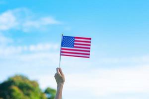 Hand, die die Flagge der Vereinigten Staaten von Amerika auf blauem Himmelshintergrund hält. usa feiertag von veteranen, denkmal, unabhängigkeit und arbeitstagkonzept foto