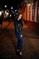 Nachtporträt von Mädchen Model Wear auf Brille, Jeans und Lederjacke, mit Rucksack, gegen die Straßen der Stadt. foto